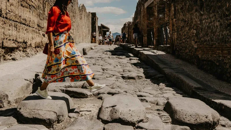 Woman in a long dress crossing the stepping stones of a Pompeii street on guided Pompeii tours from Rome by fast train, Campania, Italy